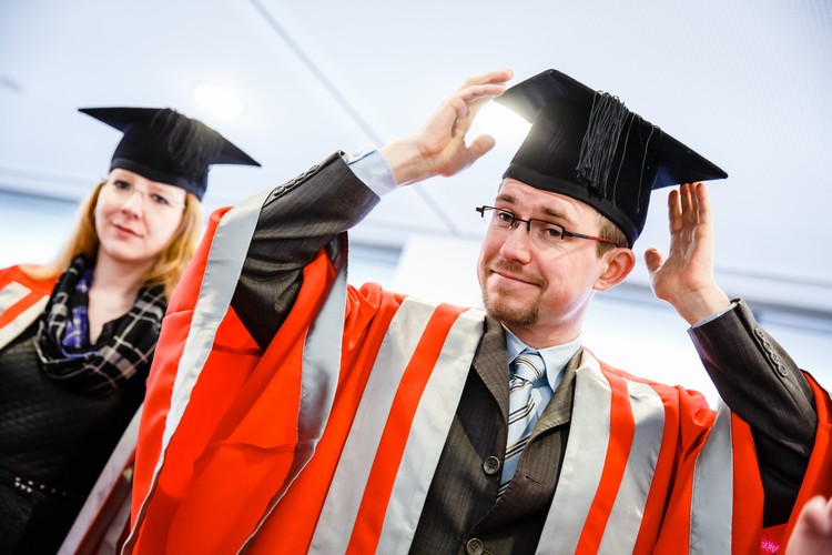 A graduate placing a motarboard on his head with a slight smile on his face