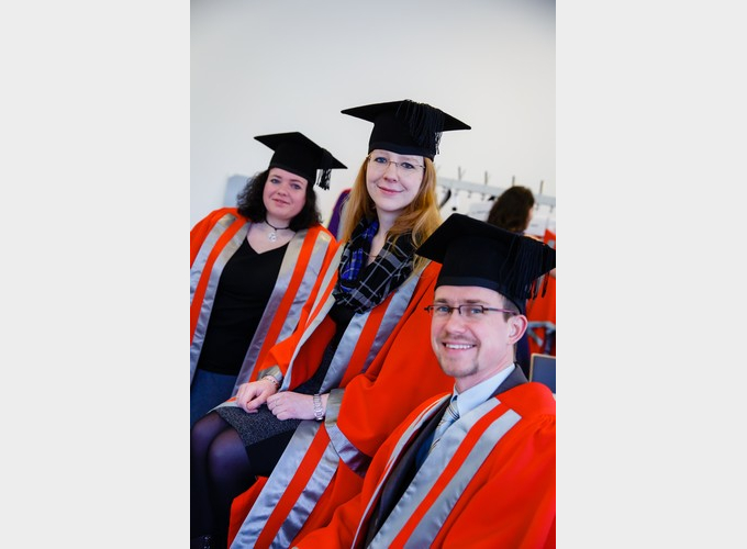 Three graduate in motarboards and gown looking at the camera and smiling