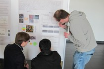 Three people inspecting a poster in some detail