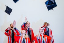 Five graduates tossing their mortarboards in the air.