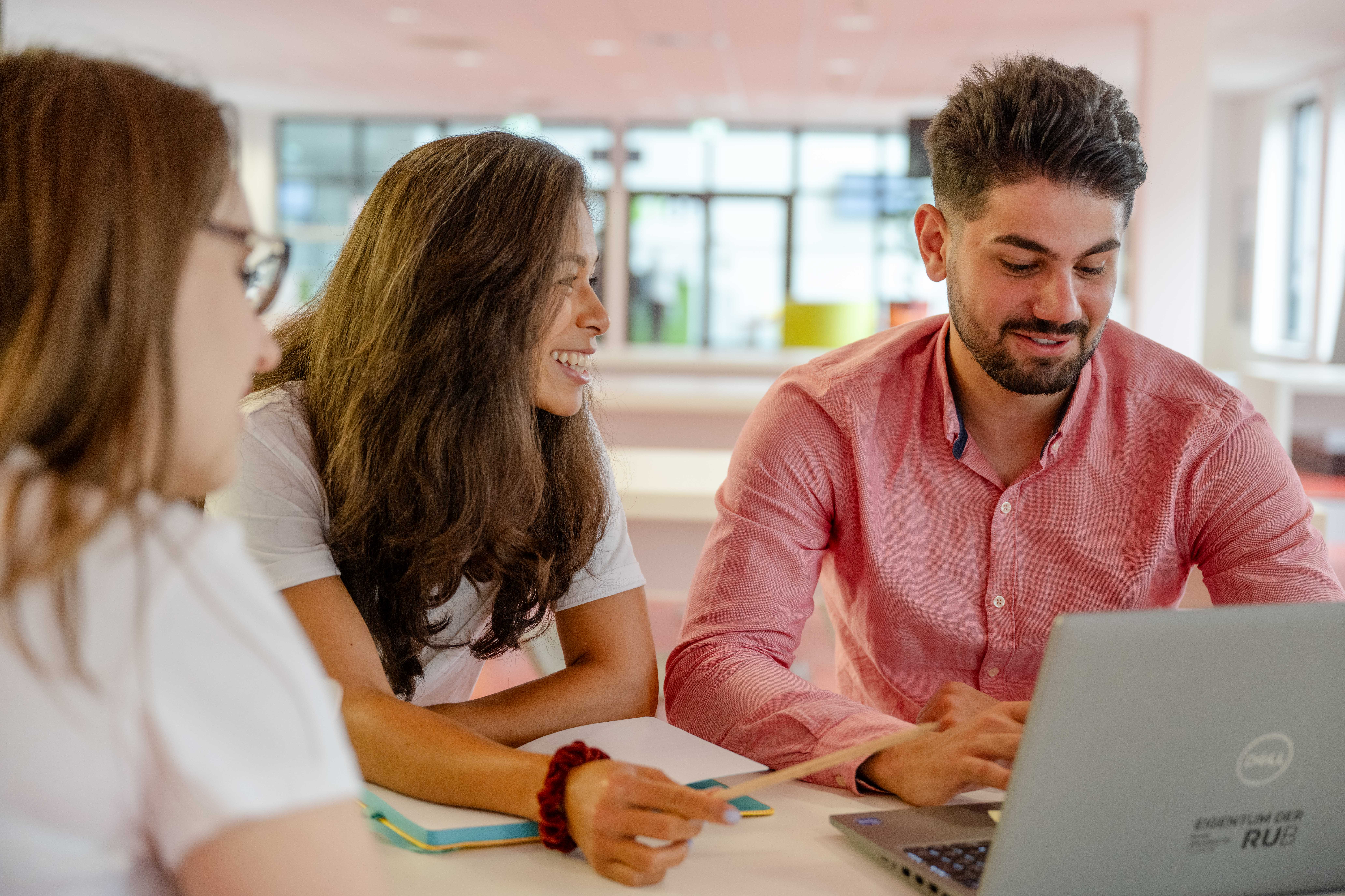 Zwei Studentinnen und ein Student mit Laptop im Gespräch
