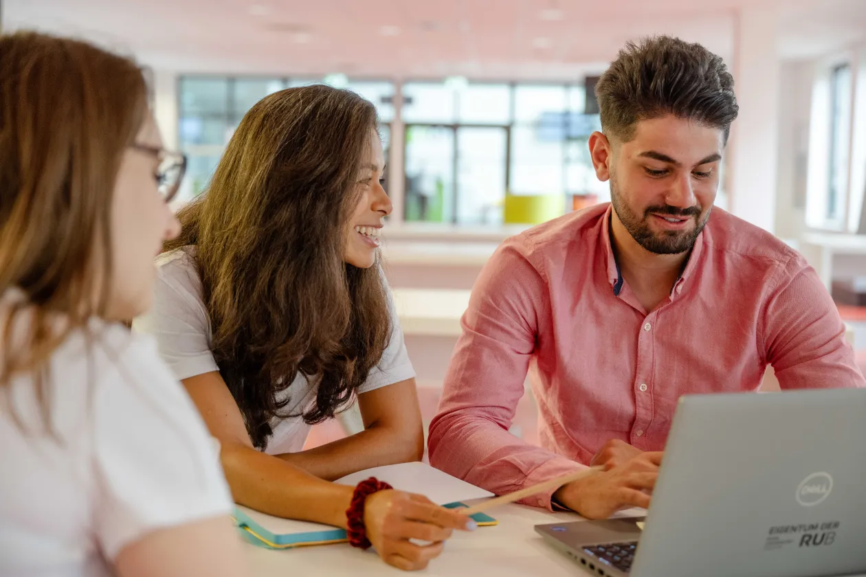 Zwei Studentinnen und ein Student mit Laptop im Gespräch