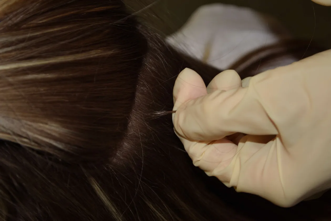 Eine behandschuhte Hand greift eine Haarsträhne