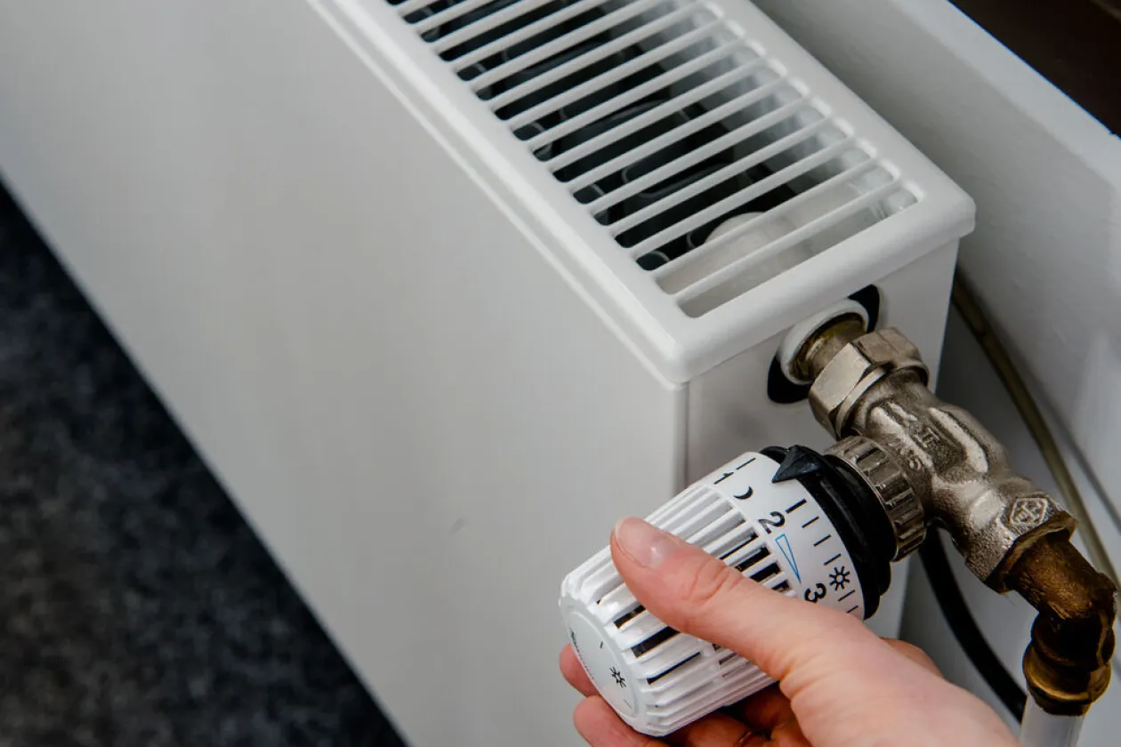 Hand am Thermostat eines Heizkörpers