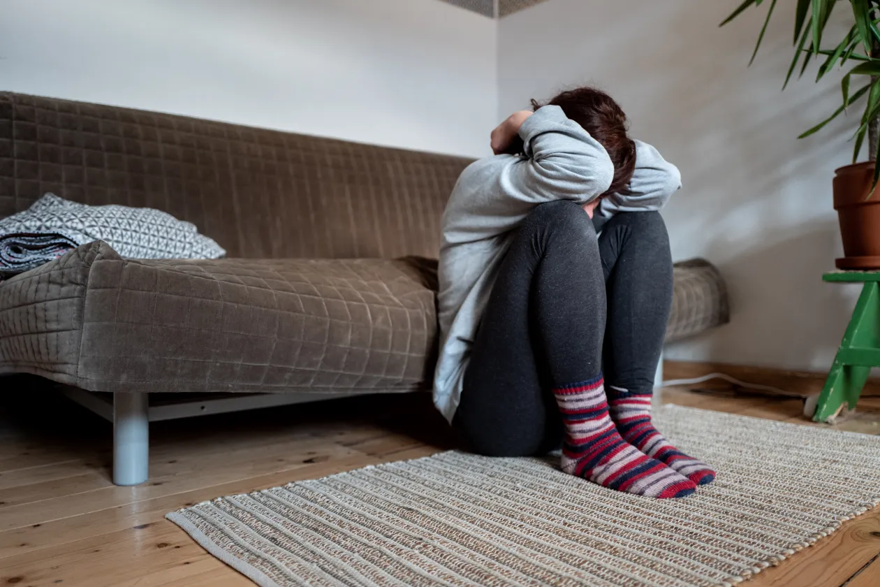 Eine Frau hockt vor einem Sofa und hält ihren Kopf zwischen den Armen