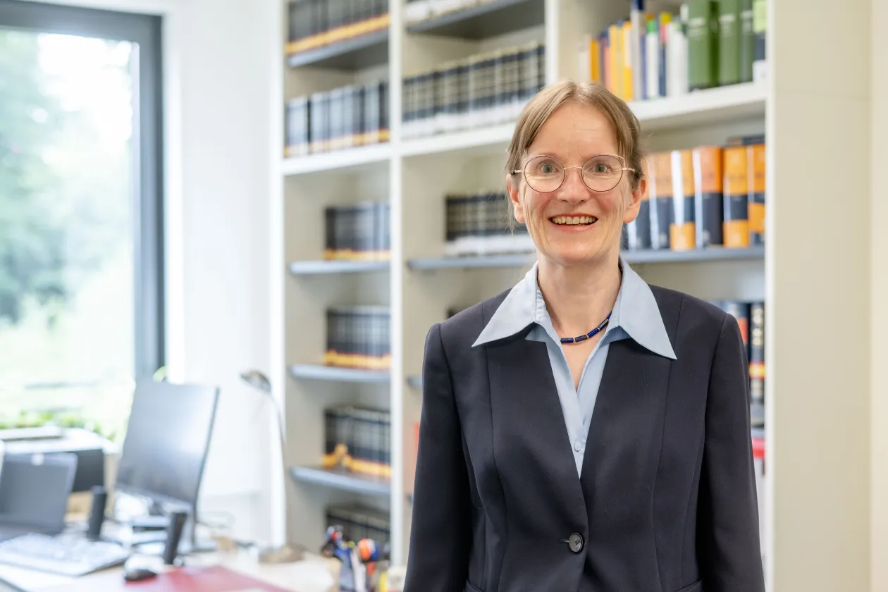Eine Frau im dunkelgrauen Jackett vor einer Bücherwand