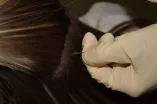 Eine behandschuhte Hand greift eine Haarsträhne