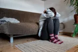 Eine Frau hockt vor einem Sofa und hält ihren Kopf zwischen den Armen