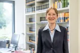 Eine Frau im dunkelgrauen Jackett vor einer Bücherwand