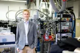 Ein Mann im grauen Jackett steht vor einer Laboranlage