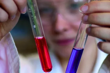 Schüler hält zwei Reagenzgläser mit roter und blauer Flüssigkeit in die Kamera.