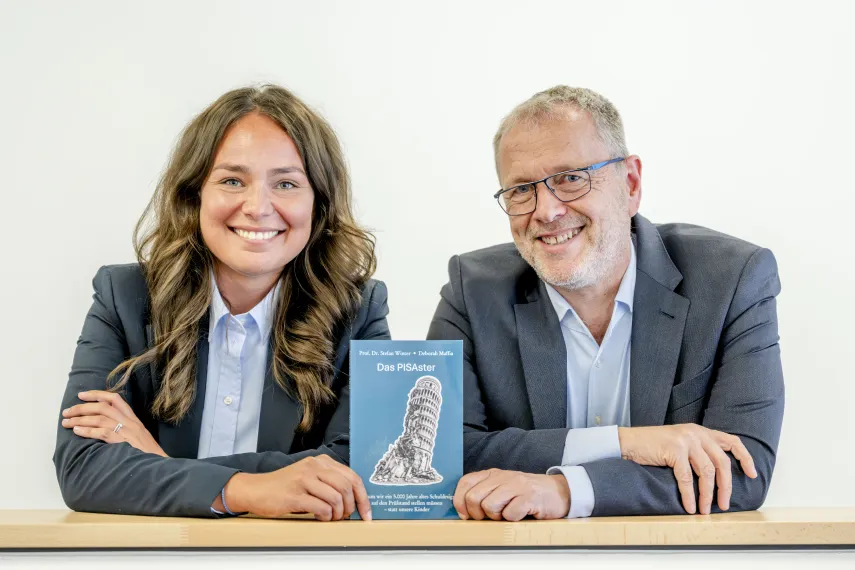 Eine Frau und ein Mann halten ein Buch aufrecht in die Kamera